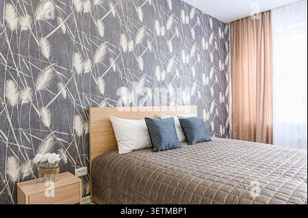 Cozy bedroom with a bed, patterned wallpaper, and side table with flowers.  Warm lighting and soft textures create an inviting space Stock Photo