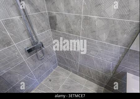 Modern shower with gray textured tiles, geometric patterns on the upper part, and a metallic showerhead. The floor is also tiled in gray with white ve Stock Photo