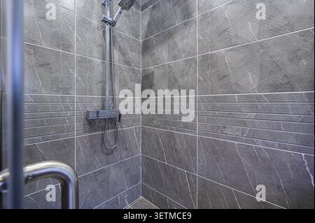 A modern shower stall with gray, patterned tiles and a chrome shower fixture. The tile design features geometric shapes and horizontal accents Stock Photo