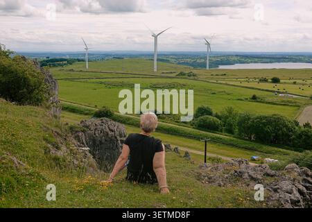 A woman sitting on Harboro Rocks, enjoying the panoramic view of wind turbines and Carsington Water, Derbyshire, England. Stock Photo