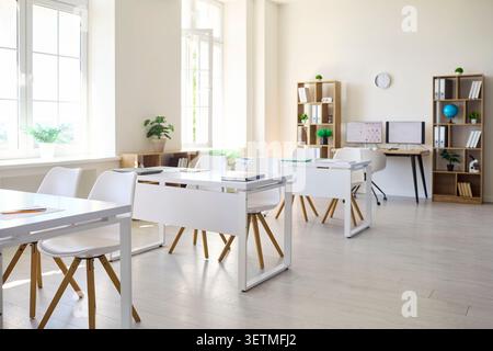 Bright modern classroom interior with white desks, chairs, shelves and computer Stock Photo