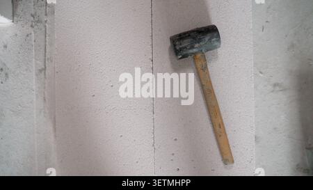Rubber mallet with wooden handle leaning against rough concrete surface. Soft directional lighting creates subtle shadow. Neutral gray beige tones. Mi Stock Photo