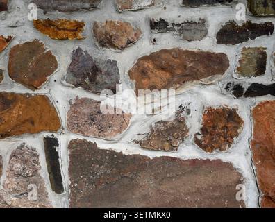 Close up of a rock and mortar wall surface with porous uneven stones, thick cracked light gray mortar joints Stock Photo