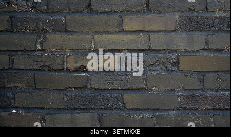 Close up of a weathered painted black reclaimed brick and mortar wall surface with chipped uneven bricks, porous thick mortar joints Stock Photo
