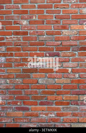 Close up of a weathered red brick and mortar wall surface with rough uneven bricks in varied red shades Stock Photo