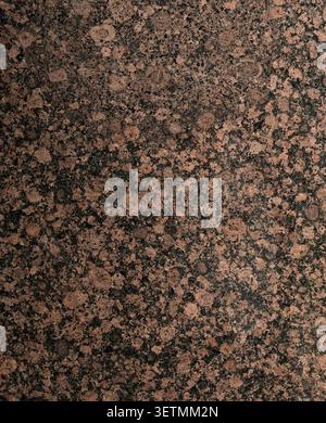 Vertical close up of polished reddish brown granite with black rounded blotches, crater‑like circular forms, gray patchy areas Stock Photo