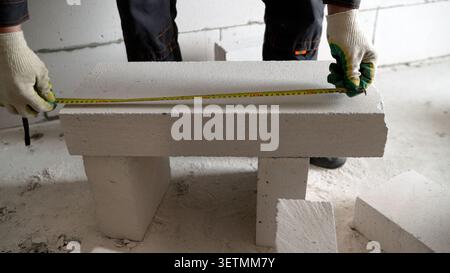 A builder uses a tape measure at a construction site. During the process of insulating walls at a construction site to cut the required size of the sl Stock Photo