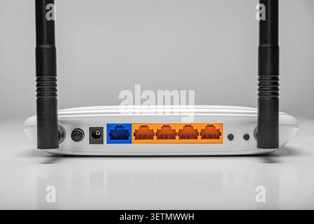 A white internet router with two black antennas shows its back panel featuring colorful Ethernet and WAN ports against a clean light background. Stock Photo