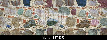 Stone wall made of large colored natural stones in gray mortar Stock Photo