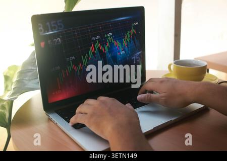 Business Analyst Working on Laptop with Stock Market and Cryptocurrency Trading Chart on Screen in Modern Home Office Stock Photo