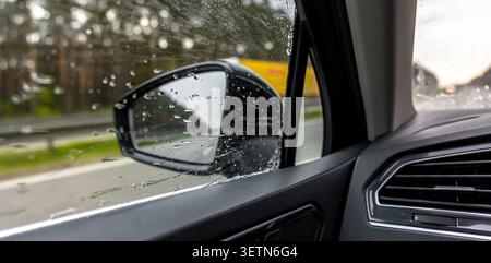 Rain on car side window. Mirror and wet road driving content. Stock Photo