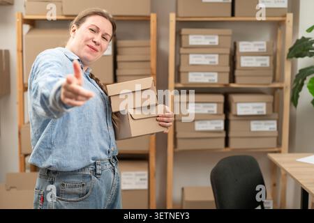 Caucasian entrepreneur. Small business owner. Standing in a warehouse, pointing her index finger directly at the camera with a cheerful smile, as if t Stock Photo