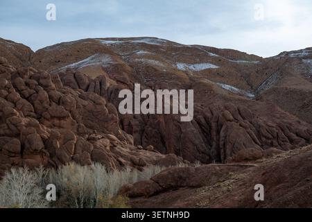 Monkey Finger Canyon features rugged reddish rock formations, sparse winter vegetation, and patches of snow beneath a pale overcast sky. Stock Photo