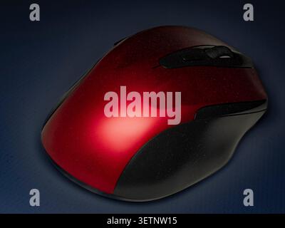 Macro studio shot of an ergonomic red and black metallic computer mouse resting on a textured dark blue surface Stock Photo