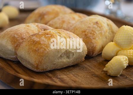 Fresh baked golden brown bread rolls served on a wooden tray with butter at a catered special event. Stock Photo