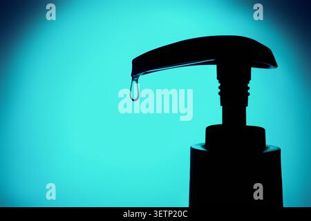 Soap dispenser head in silhouette dispensing single drop of liquid on turquoise background Stock Photo