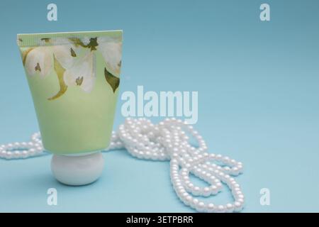 Hand cream tube with jasmine flowers and pearl necklace on blue background Stock Photo