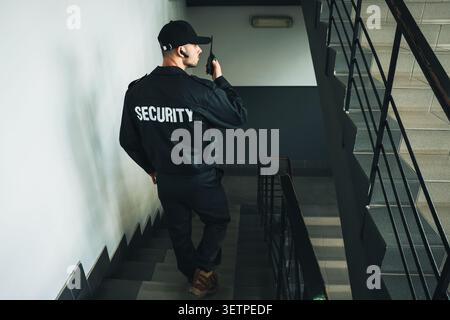 Bodyguard in uniform using walkie talkie while walking down stairs indoors Stock Photo