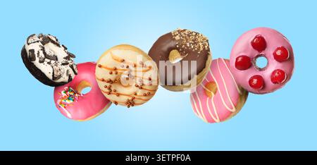 Yummy donuts covered with icing falling on light blue background Stock Photo