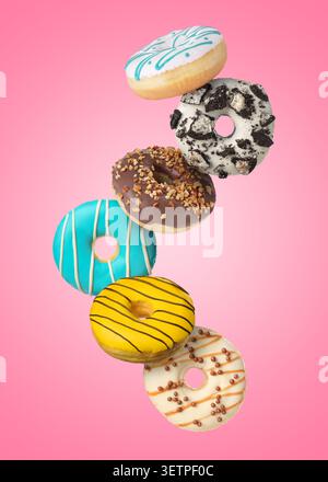 Yummy donuts covered with icing falling on pink background Stock Photo