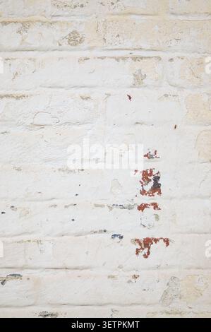 Old painted brick wall featuring cracked white paint and exposed masonry. Industrial grunge texture with copy space. Stock Photo