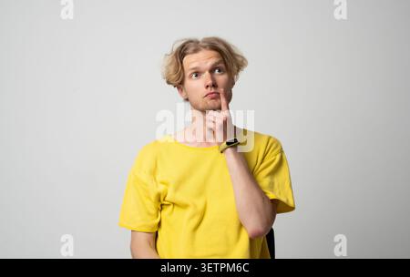 Thoughtful young man in yellow t-shirt thinking and contemplating, looking up and making decisions with a curious facial expression, finding solutions Stock Photo