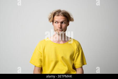 Young man showing confusion and doubt, biting lower lip and looking away, pondering with a thoughtful facial expression, expressing hesitation and Stock Photo