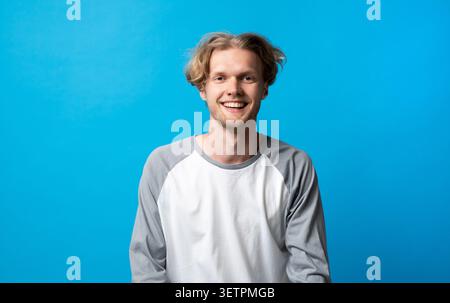 Smiling young blonde man radiating happiness and joy, looking directly at the camera with a cheerful expression, wearing a casual long sleeve shirt on Stock Photo
