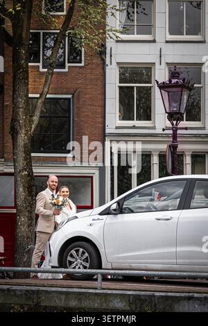 Bride and groom with a bouquet walking against the background of traditional old buildings and trees. Stock Photo