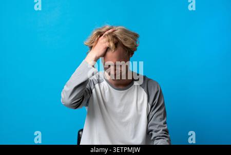 Young man experiencing severe headache, stress, and frustration, grimacing and holding his head in discomfort, suffering from pain and mental distress Stock Photo