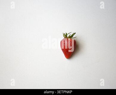 Top view of a single fresh ripe strawberry placed on a clean white table, creating a minimalist composition ideal for healthy eating, organic produce, Stock Photo