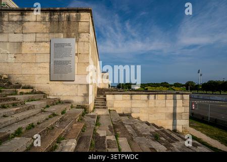 Detail of a historical metal plaque mounted on the limestone wall at the Zeppelinfeld in Nuremberg. The shot captures the weathered stone steps, a mon Stock Photo