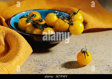 Yellow cherry tomatoes in ceramic bowl on yellow fabric surface Stock Photo