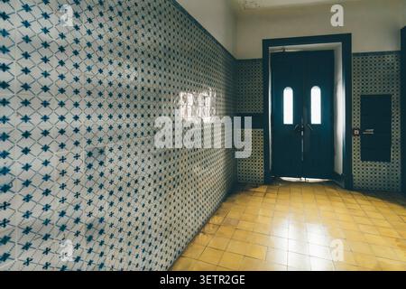 Historic apartment entryway in Lisbon with blue azulejo wall tiles, yellow ceramic floor and dark double doors, atmospheric Portuguese interior Stock Photo