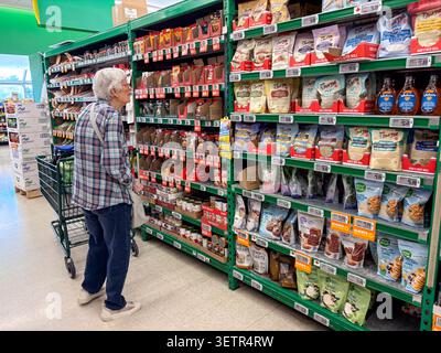 An elderly woman standing in a supermarket aisle examining a shelf of packaged food products. Stock Photo