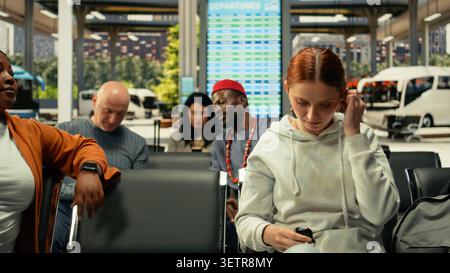 Close up of woman using headphones while waiting on metropolitan bus ride, using public transportation line during rush hour. Convenient everyday travel in modern bus station. Stock Photo