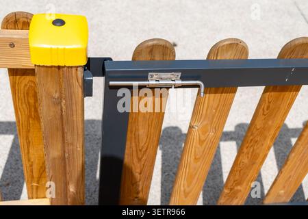 Detailed view of a sturdy wooden fence section featuring a metallic slide bolt latch and a bright yellow protective cap on a post Stock Photo