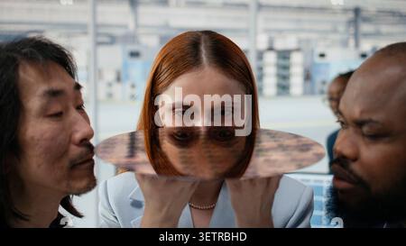 Close up of semiconductor substrate, assessing materials quality and multiethnic technicians in factory office. Studying silicon wafer, electronics and diverse coworkers squinting eyes, camera A Stock Photo
