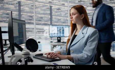 Man and woman review microchip production operations inside factory workplace with PC software. Experts in RD office working to improve semiconductor hardware performance, camera A Stock Photo