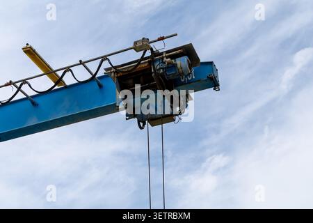 The image showcases an industrial crane lifting equipment, highlighting its machinery and cables against a clear blue sky Stock Photo
