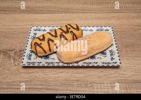 Two elongated pepitas pastries with sugar coating and chocolate drizzle rest on a decorative blue and white rectangular plate. Stock Photo