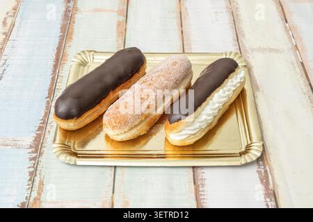 Oblong sugar-dusted and chocolate-drizzled pastries sit arranged on a rectangular ceramic plate with blue floral patterns over wood. Stock Photo