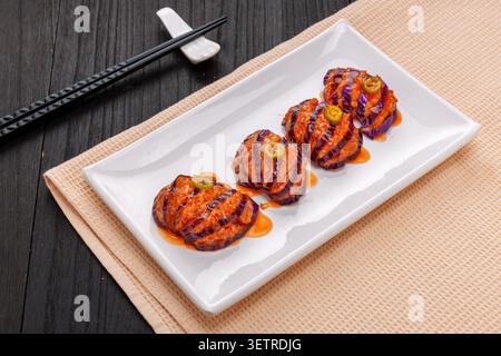 Traditional Chinese sweet and sour sauce stuffed lantern eggplants with pork, served on a white rectangular plate with chopsticks on a dark wooden bac Stock Photo