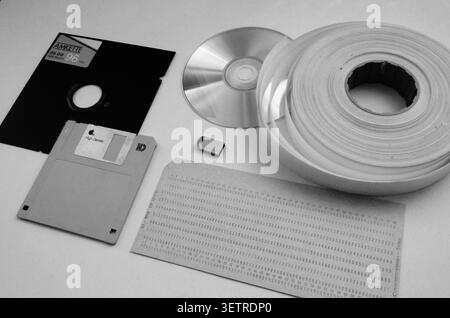Black and white evolution of data storage: vintage floppy disks, CD, magnetic tape reel, and computer punch card, retro technology concept Stock Photo