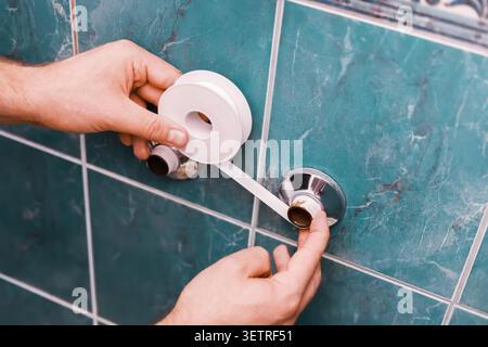Homeowner replacing an old faucet during a DIY plumbing repair. Hands applying thread sealant tape on pipes for a bathroom home renovation. High quali Stock Photo