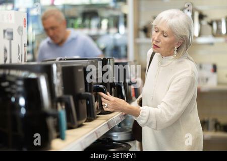 Elderly woman choosing air fryer at household appliances store Stock Photo