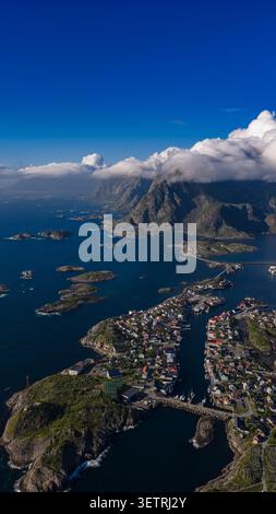 Aerial view of Lofoten Islands featuring dramatic jagged peaks, turquoise waters, scattered islands, and colorful waterfront village Stock Photo