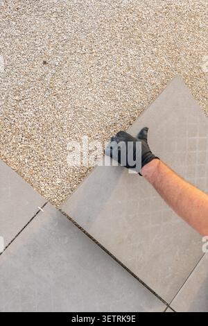 Laying tiles on gravel base.Worker placing large paving slabs on prepared gravel base for terrace construction.Installing patio tiles on gravel base Stock Photo