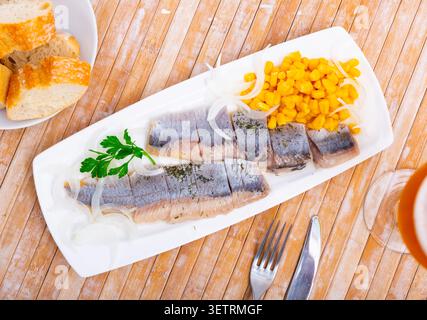 Sliced pickled herring fillet with corn and onions on plate Stock Photo