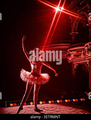 Ballerina poised beneath  radiant red stage light inside ornate theater, dramatic lens flare, architectural elegance creating striking performance Stock Photo